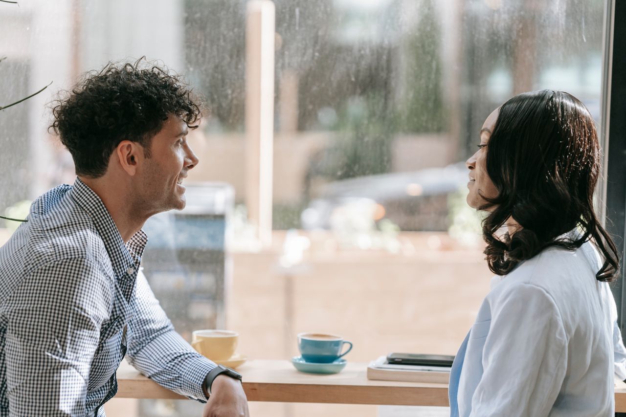 Two colleagues conversing over coffee by a window, enjoying a relaxed break indoors.
